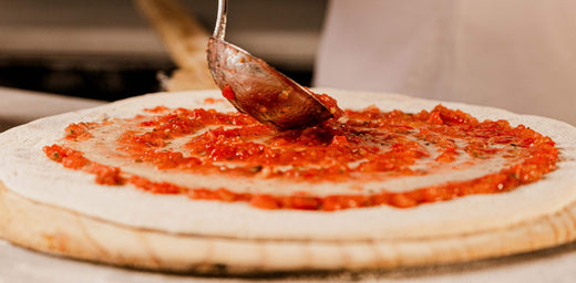 Person spreading pizza sauce on pizza dough