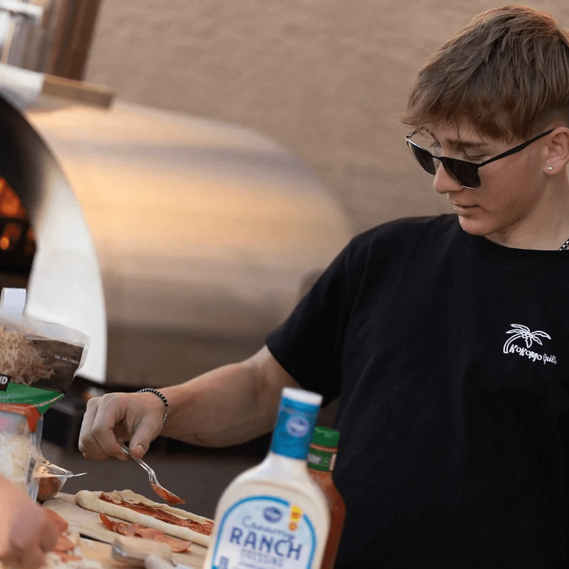 Person making pizza using a Kokomo Grills Outdoor Pizza Oven